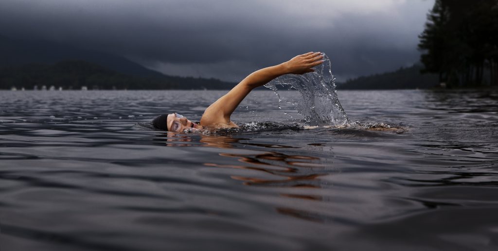 Someone swimming in a lake, taking a big breath as their arm moves overhead