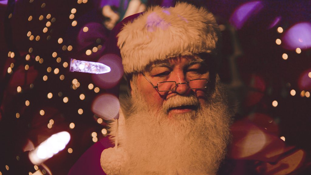 A close up of Santa's face with twinkly lights in the background