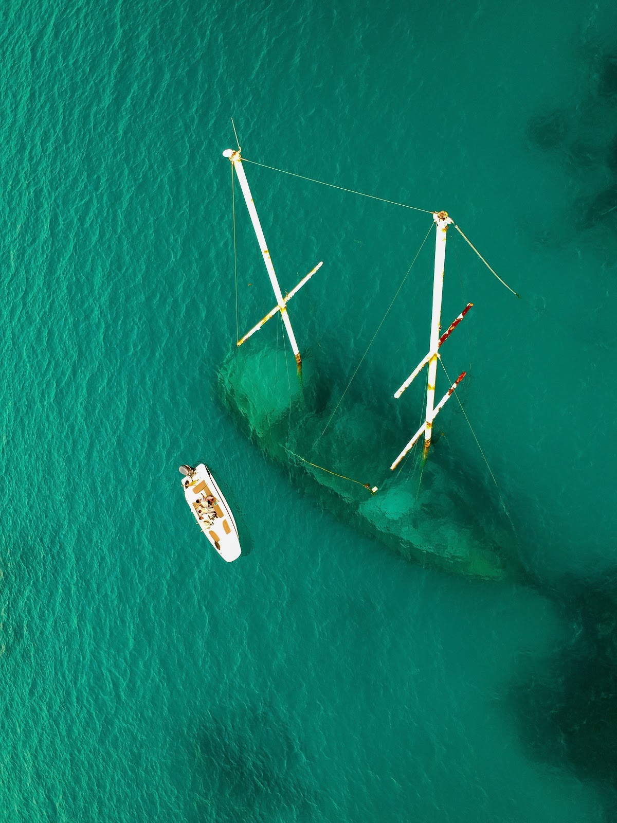 A small boat sails by a larger boat that is almost completely submerged in the ocean.